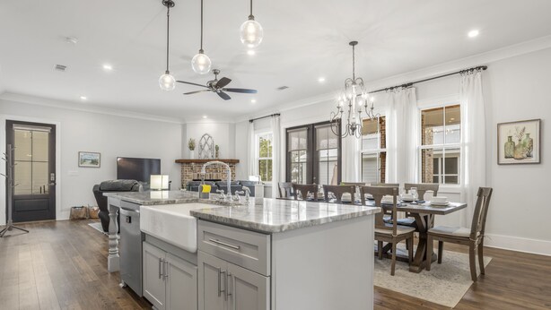 A modern kitchen with a central island, wooden flooring, and pendant lighting.