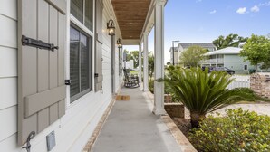 A covered porch with a wooden ceiling, a bench, and a small palm tree.