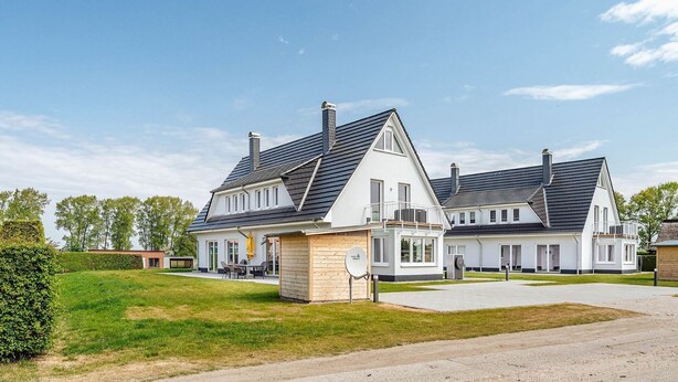 A modern two-story house with a large driveway and a well-maintained lawn. - Zur Oie 27 "Westwind" (left) - Holiday home close to nature (Pruchten)