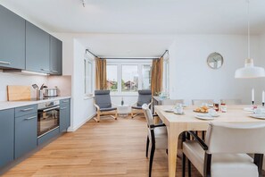 Eine moderne Küche mit grauen Schränken, einer Holz Arbeitsplatte und einem Essbereich mit einem Tisch für zwei Personen.