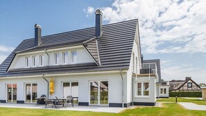 A large, modern house with a sloped roof, multiple windows, and a covered patio area with outdoor furniture. - Zur Oie 27 "Westwind" (left) - Holiday home close to nature (Pruchten)