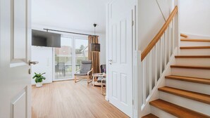 A modern interior with a staircase, a flat-screen TV, and a dining area with a table and chairs. - Zur Oie 27 "Westwind" (left) - Holiday home close to nature (Pruchten)