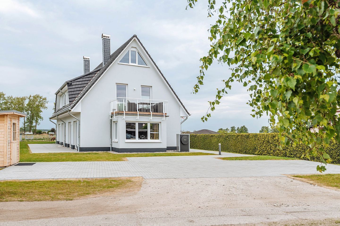 Une maison à deux étages avec un balcon, un petit abri de jardin et une allée pavée.