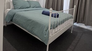 A bedroom with a white metal bed frame, teal bedding, and a dark carpet. - Modern House in Newton (Newton)