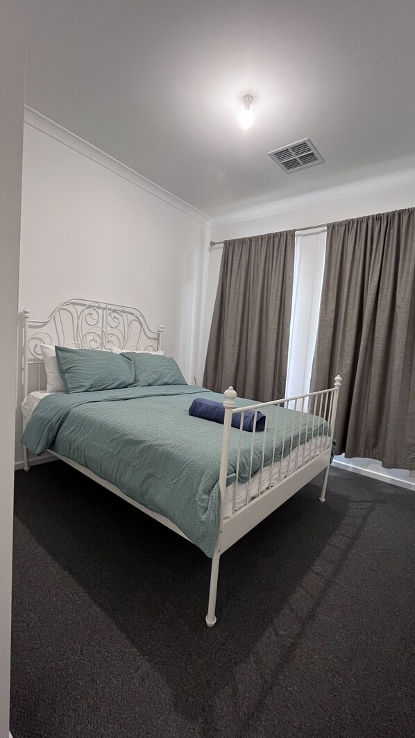 Ein Schlafzimmer mit einem Bettgestell aus weißem Metall, türkisblau gestreuter Bettwäsche und einem dunklen Teppich.