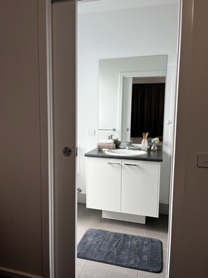 A modern bathroom with a white vanity, a large mirror, and a dark bath mat. - Modern House in Newton (Newton)