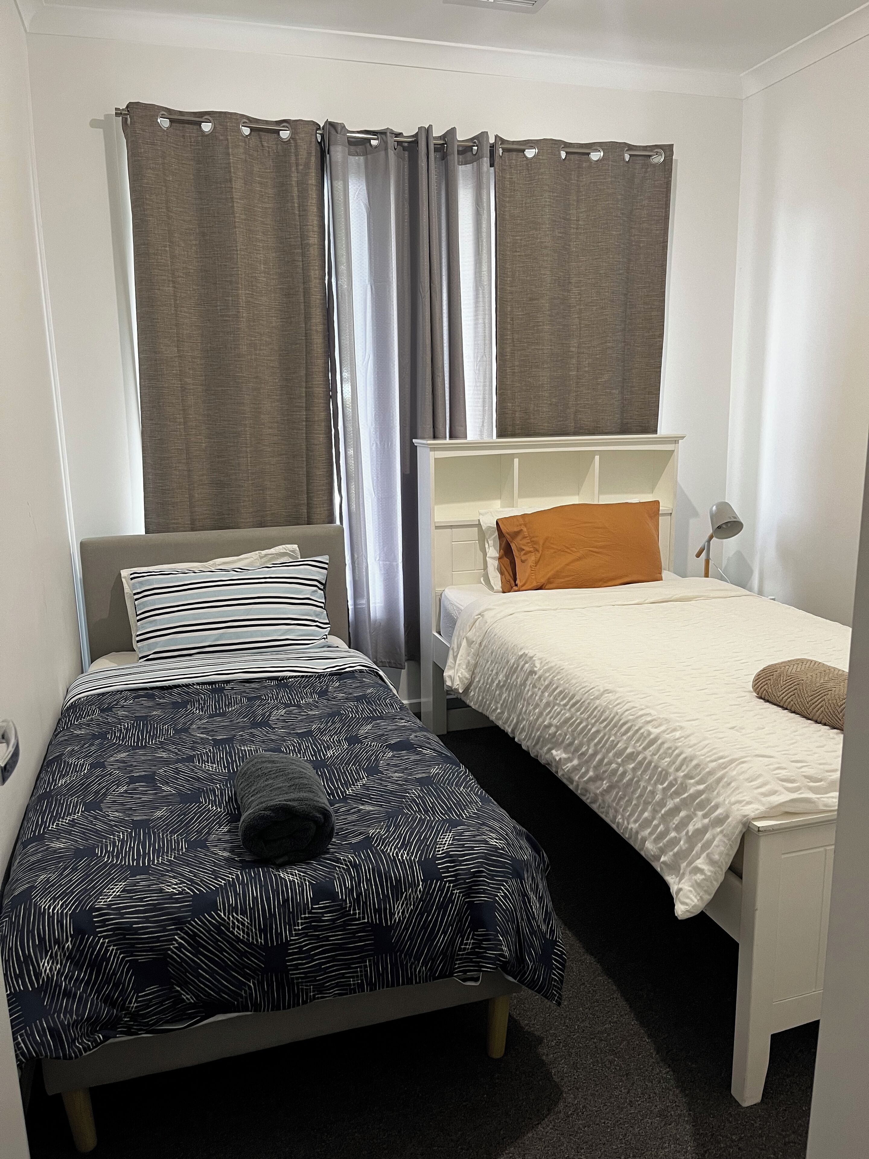 A bedroom with two beds, a window with curtains, and a bedside lamp.