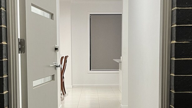 A hallway with a door on the left, a window with a blind on the right, and a doormat at the end. - Modern House in Newton (Newton)