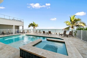 A swimming pool with lounge chairs and palm trees, surrounded by a white fence.