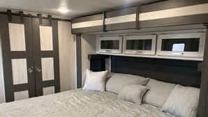 A bedroom with a bed, a wardrobe, and a headboard with built-in lighting. - 10 minutes walk to the beach .Covered rv spot on concrete slab. NEW CAMPER (Bolivar Peninsula)