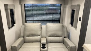 A room with two leather recliner sofas, a window with horizontal blinds, and wall-mounted speakers. - 10 minutes walk to the beach .Covered rv spot on concrete slab. NEW CAMPER (Bolivar Peninsula)