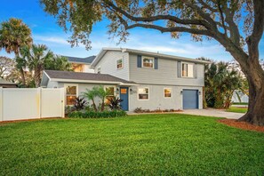A two-story house with a garage, surrounded by a well-maintained lawn and palm trees.