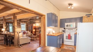 Ein rustikales Blockhaus-Interieur mit einem Holzespeisesaal, einer Küche mit blauen Schränken und einer gemütlichen Wohnbereitschaft mit einer Couch und Kamin.