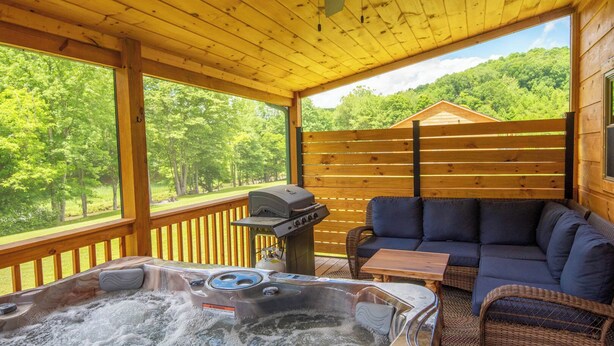 A covered outdoor area with a hot tub, a barbecue grill, and a seating area with a sofa and table. - Jones River Cabin | Riverfront Stay with Hot Tub | Near West Jefferson (Creston)