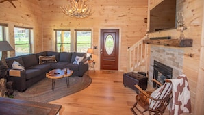 A cozy cabin interior with a wooden interior, a fireplace, a sofa, and a television mounted on the wall. - Jones River Cabin | Riverfront Stay with Hot Tub | Near West Jefferson (Creston)