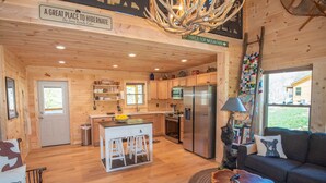 A cozy cabin interior with a wooden interior, a kitchen area, a dining space, and a seating area with a couch and a table. - Jones River Cabin | Riverfront Stay with Hot Tub | Near West Jefferson (Creston)
