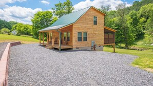 A wooden cabin with a porch, a covered deck, and a gravel driveway. - Jones River Cabin | Riverfront Stay with Hot Tub | Near West Jefferson (Creston)