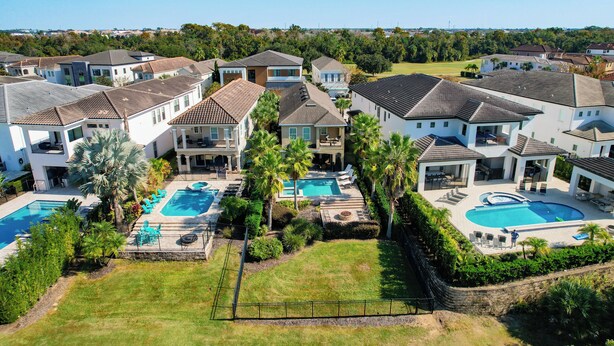 Un área residencial con varias casas, una piscina grande y jardines bien cuidados.