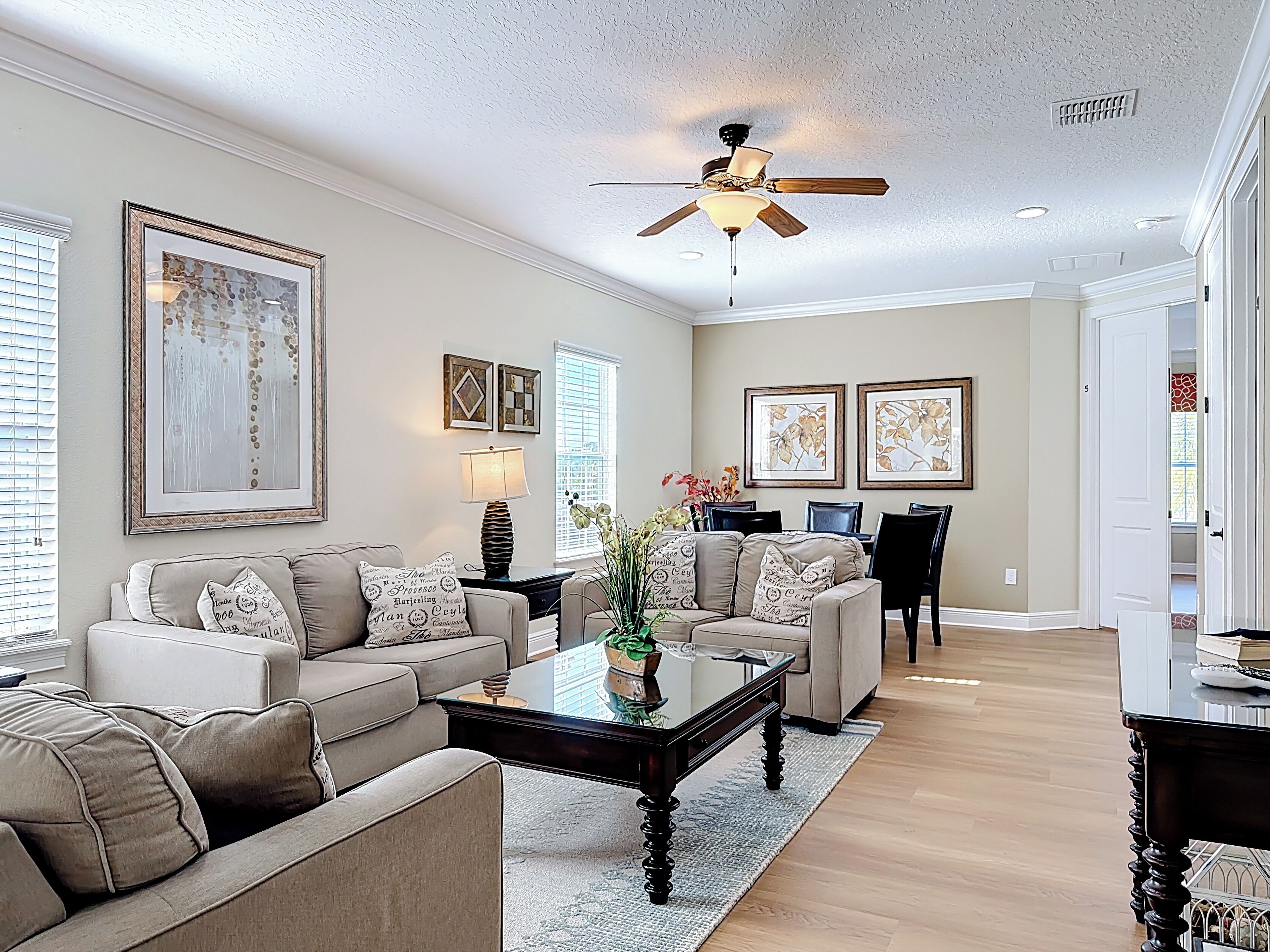 A spacious living room with a ceiling fan, a dining area with chairs, and framed artwork on the walls.