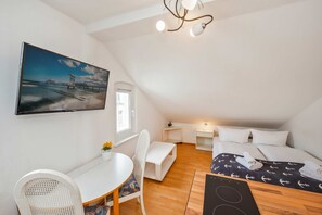 A small, cozy room with a bed, a desk, a chair, and a painting of a bridge.