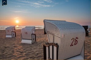 A beach with several wicker beach chairs labeled with numbers, a sunset in the background, and a calm sea.
