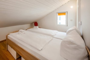 A single bed with white bedding and a wooden headboard in a room with white walls and a sloped ceiling. - Geräumiges Ferienappartement für Max. 5 Personen im Herzen von Heringsdorf - Villa Seeland (Heringsdorf)