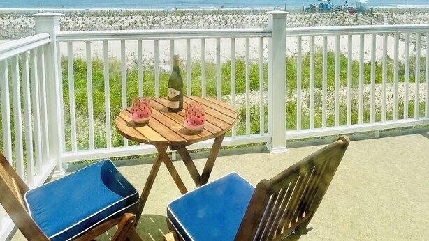 Ein Balkon mit Tisch und Stühlen mit Blick auf einen Strand.