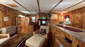 L’intérieur d’une cabane comprend un coin cuisine, un lit avec un coussin à carreaux, un banc en bois et une petite table.