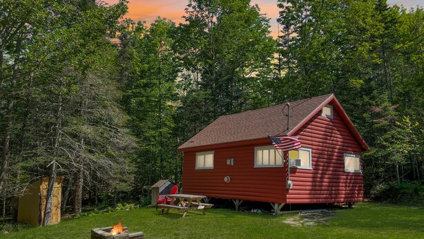 Une cabane rouge avec un foyer et une table de pique-nique, située dans une zone boisée.