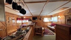 L’intérieur d’une cabane comprend un coin cuisine, des murs en bois, une table à manger, un canapé et une cheminée.