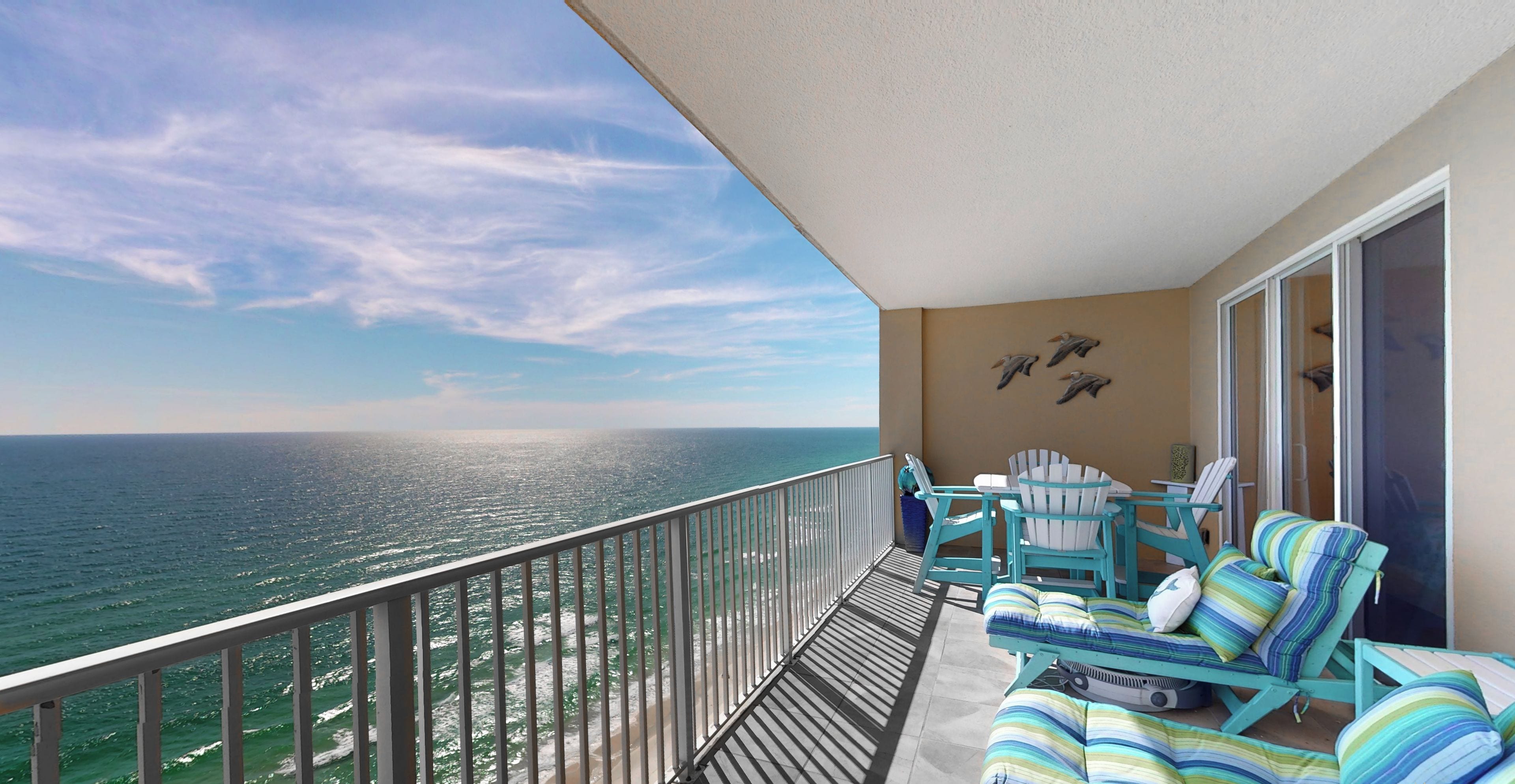 A balcony with a view of the ocean, featuring a seating area with striped cushions and a table.