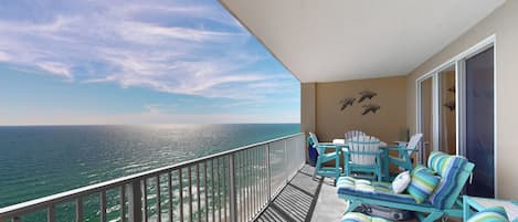 A balcony with a view of the ocean, featuring a seating area with striped cushions and a table.
