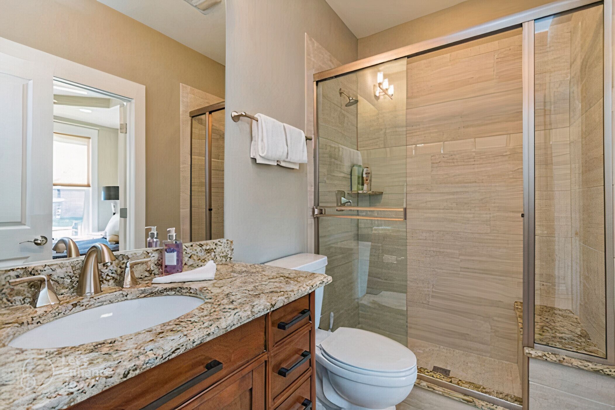 A bathroom with a granite countertop, a white sink, a glass shower enclosure, and a toilet.