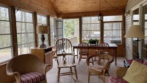 Un interno accogliente di una baita con pareti e soffitto in legno, un'area pranzo con tavolo e sedie, e un divano in vimini con un cuscino.