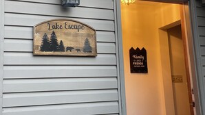 Segnaletica in legno raffigurante un orso, alberi, un lanternino e un invito a famiglie e amici a riunirsi.