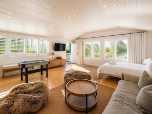 A room with a bed, sofa, futon, futon chair, wooden coffee table, and a foosball table.