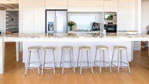 A modern kitchen with a large island, bar stools, a refrigerator, and a coffee machine.