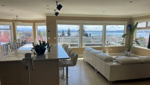 Una cocina moderna con una isla central, ventanas amplias que ofrecen vista a la ciudad y una zona de estar acogedora con un sofá blanco y una planta en maceta.