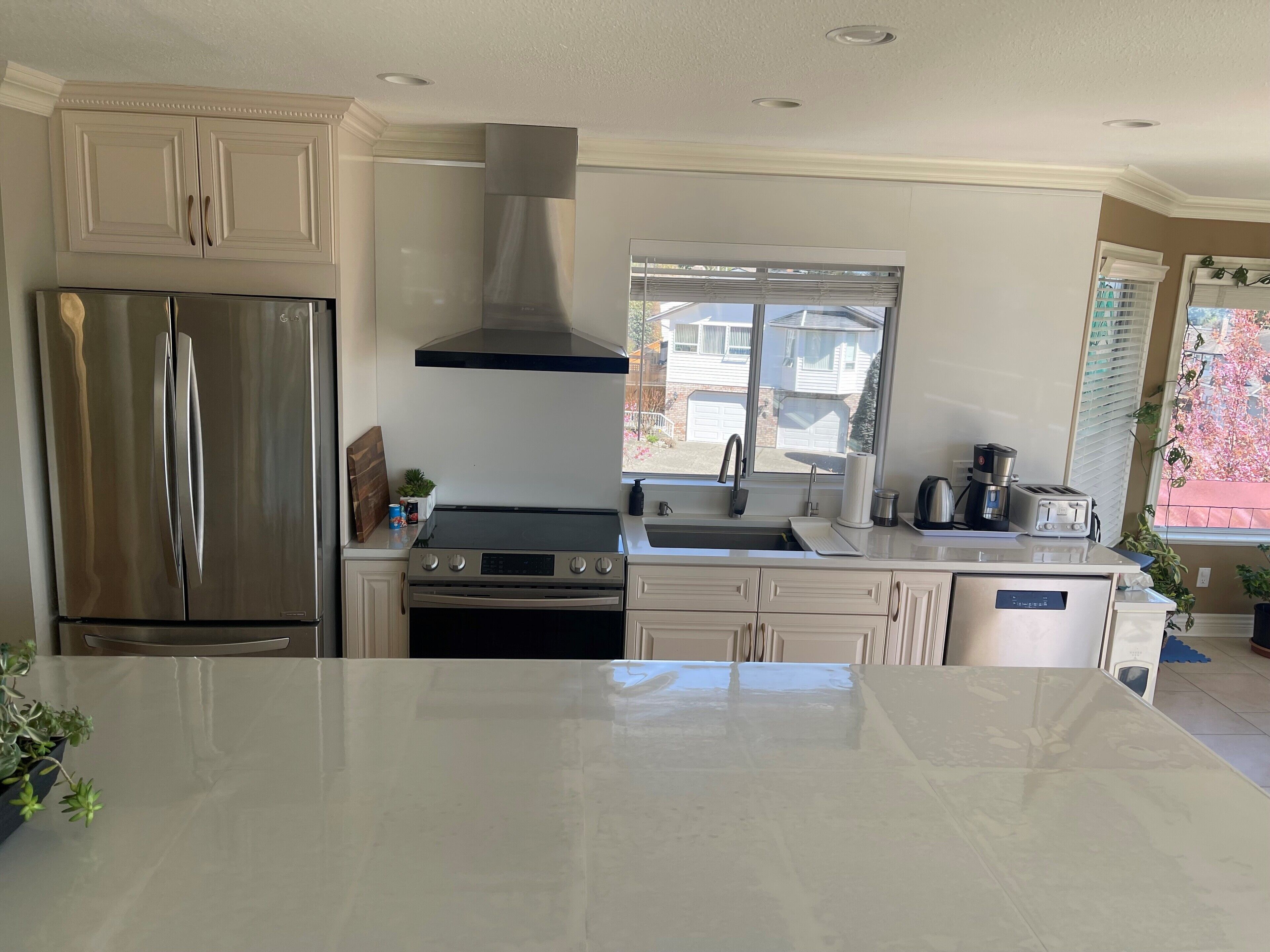 Une cuisine moderne dotée d’appareils électroménagers en acier inoxydable, d’un îlot central et d’une fenêtre laissant entrer la lumière naturelle.