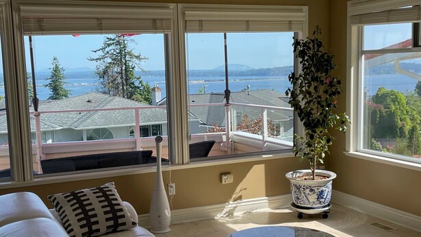 Una sala de estar con vistas a la ciudad y al mar, un sofá blanco, una mesa de centro de cristal y una planta en maceta.
