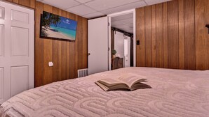 A bedroom with a bed, a painting of a beach, a white door, and a wooden wall. - Spacious & Cozy ~ Mins to Downtown (Springfield)