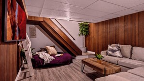 A modern living room with a sloped ceiling, wooden paneling, a sofa, a coffee table, and a bed with a purple blanket. - Spacious & Cozy ~ Mins to Downtown (Springfield)