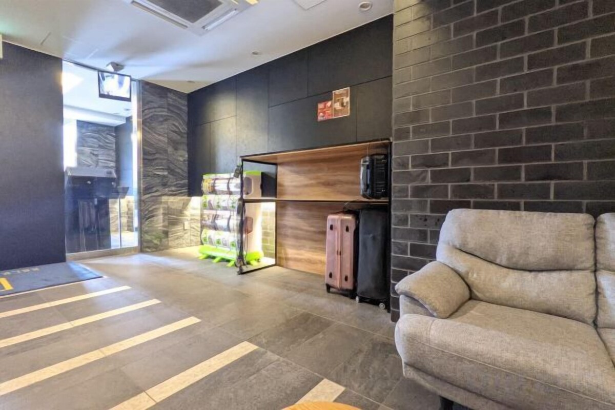 A reception area with a sofa, a luggage stand, a refrigerator, and a shelf with items.