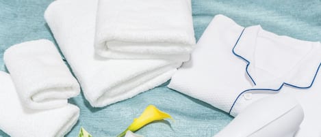 Neatly folded white towels, a white hairdryer, a yellow flower, and green plants on a blue textured surface.