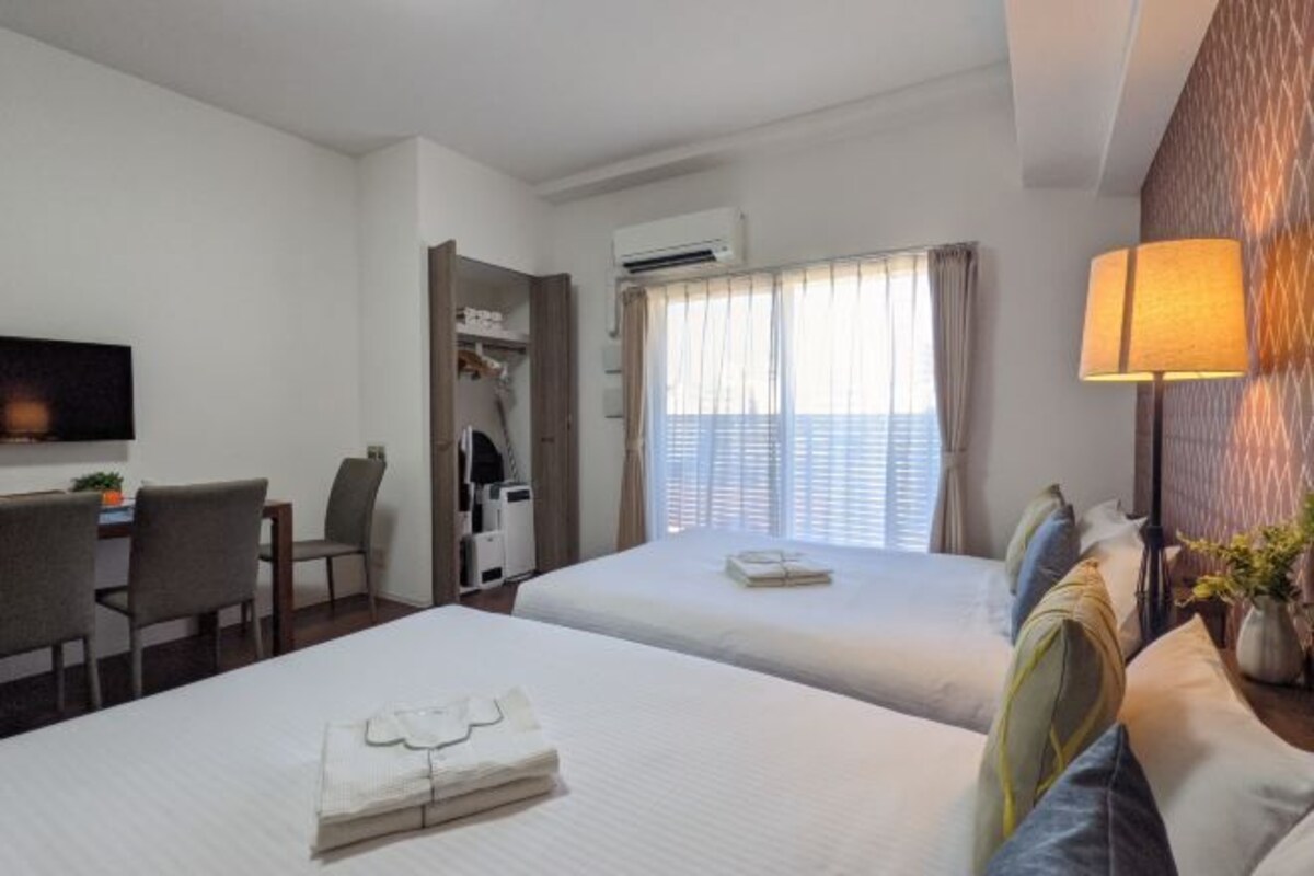 Une chambre d’hôtel avec deux lits, un bureau, une chaise, une télévision et un appareil de climatisation.
