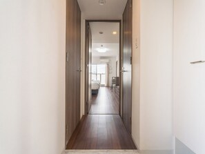 Un couloir étroit, avec des portes en bois, mène à une pièce où se trouvent un lit et une table.