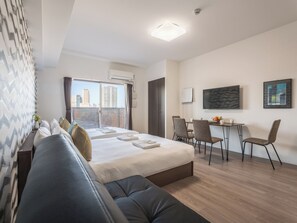A modern hotel room with a bed, a seating area, and a desk.