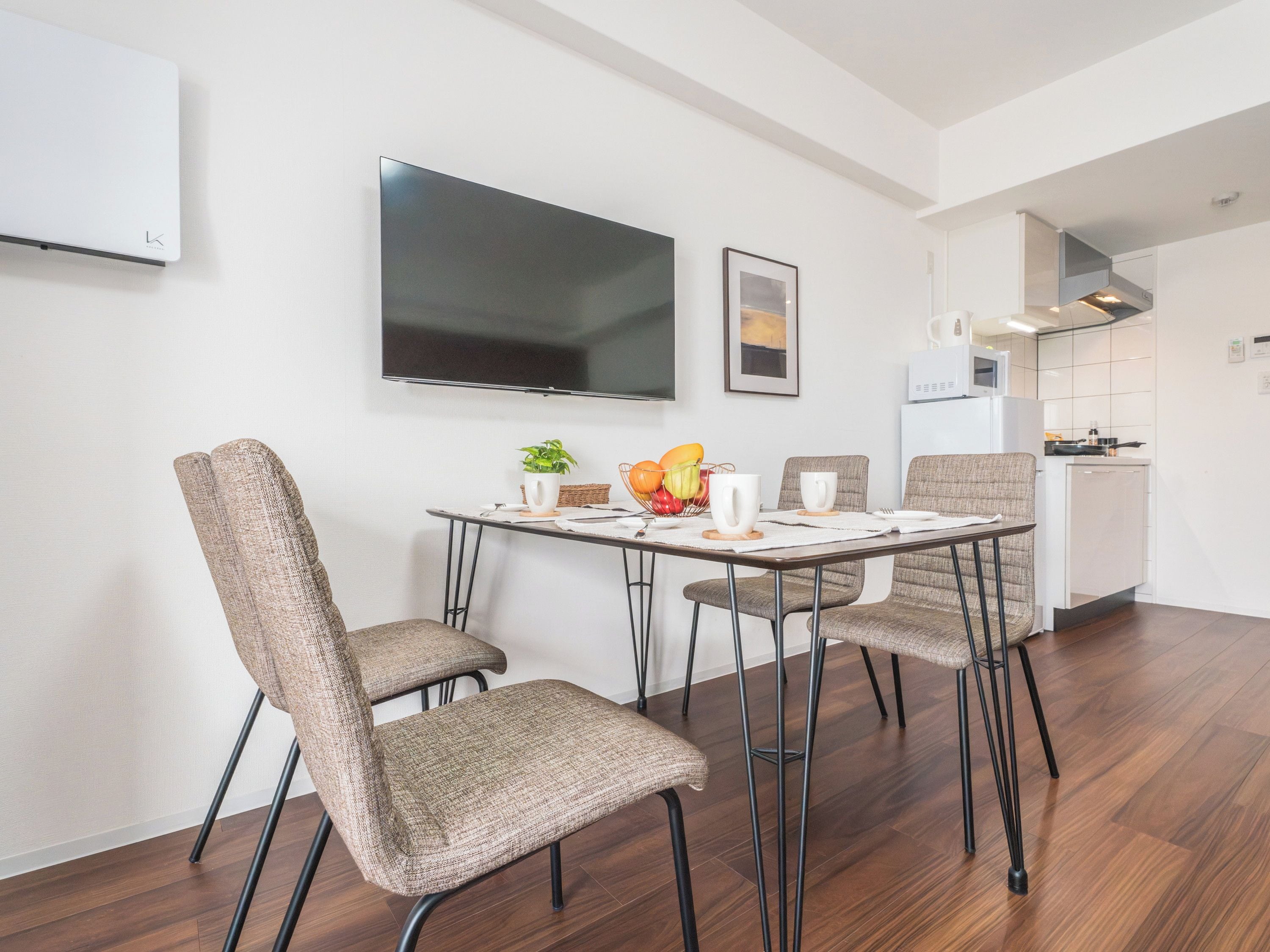 A modern dining area with a flat-screen TV, a framed picture, and a kitchen in the background.