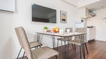 A modern dining area with a flat-screen TV, a framed picture, and a kitchen in the background.