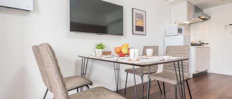 Un espace repas moderne avec un téléviseur à écran plat, un tableau encadré et une cuisine en arrière-plan.